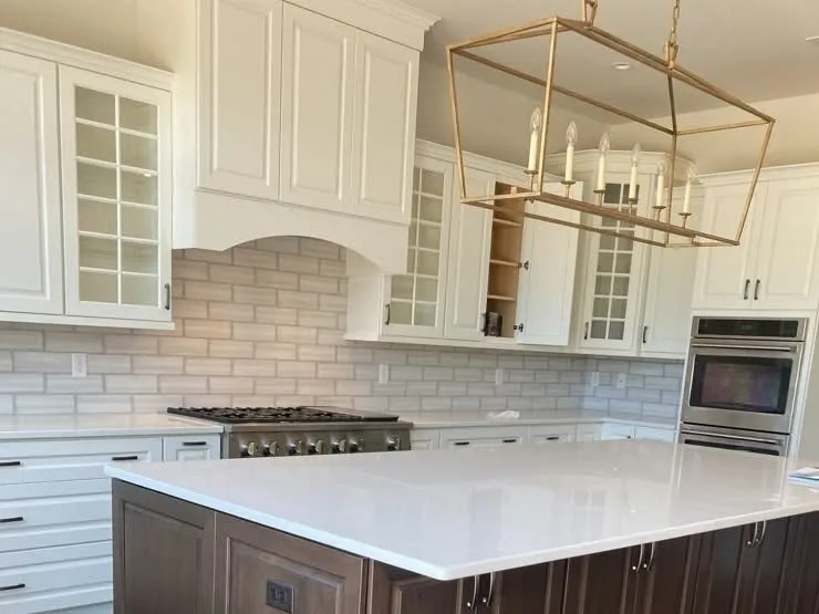 White kitchen cabinets with glass inserts and a dark wood island with a white countertop.