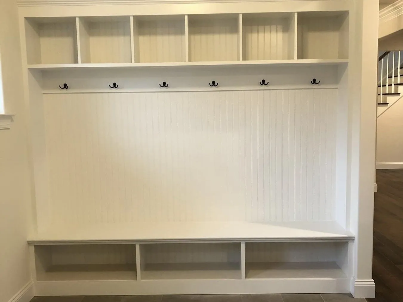 White mudroom lockers featuring overhead storage cubbies, coat hooks, and lower shoe storage compartments.