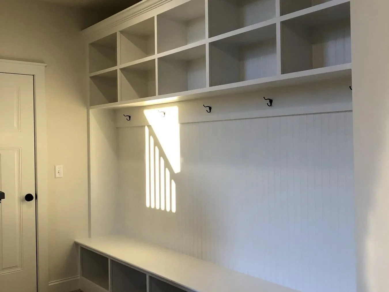 White mudroom lockers feature upper cubbies, coat hooks, and a beadboard back panel.