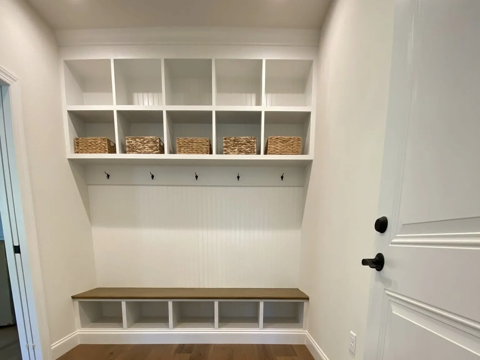 White mudroom lockers featuring upper cubbies, coat hooks, and a wooden bench with lower storage compartments.