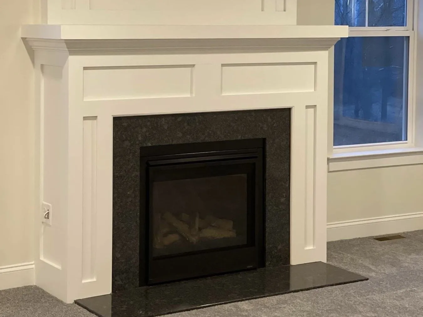 A white painted fireplace mantel surround with a dark granite hearth and fireplace insert.