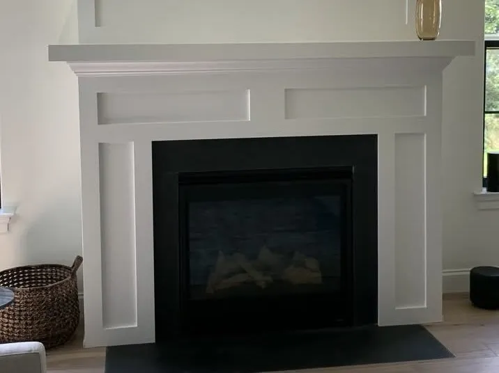 A clean white painted wood fireplace mantel with recessed panel detailing surrounding a black insert.