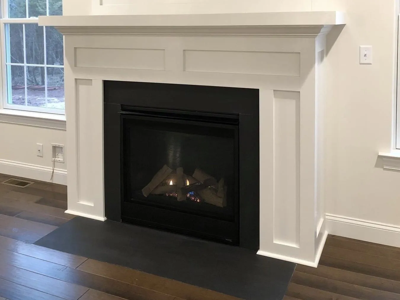 A white painted wood fireplace mantel with a black firebox and a dark hearth.
