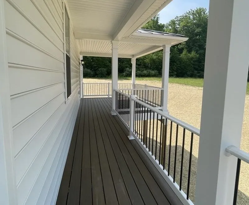 A covered porch featuring white railings with black balusters and dark composite decking boards.
