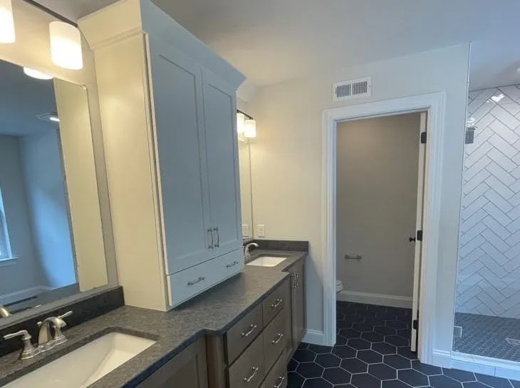 A white shaker style bathroom vanity with a tall storage tower and dark stone countertop.