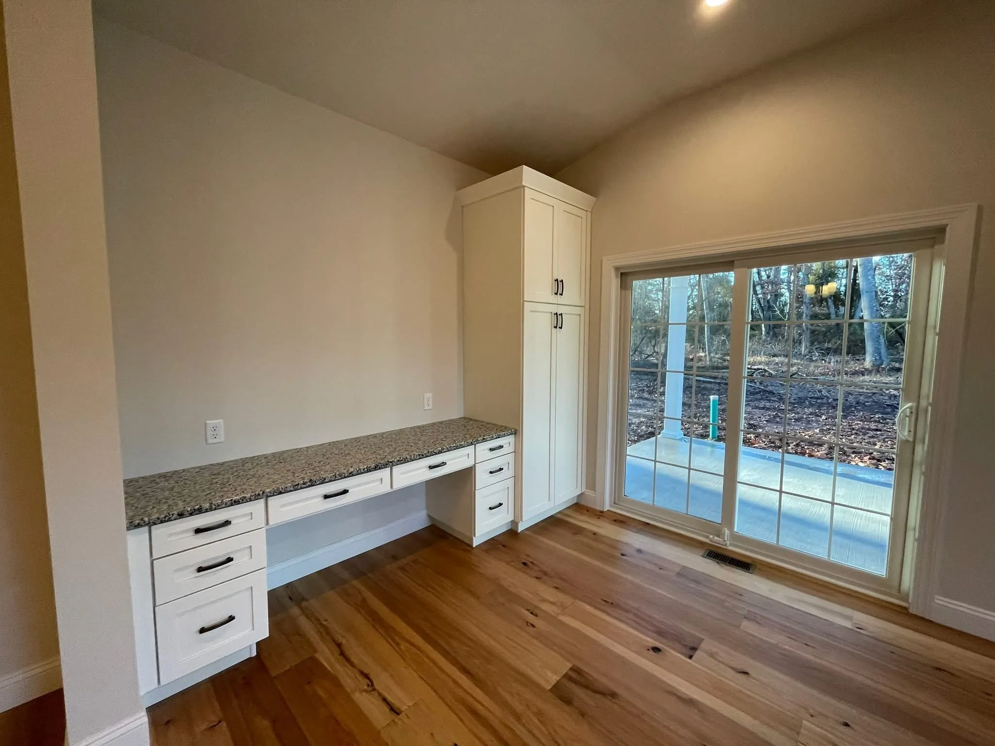 A white shaker style built-in desk with granite countertop sits against a wall next to sliding doors.