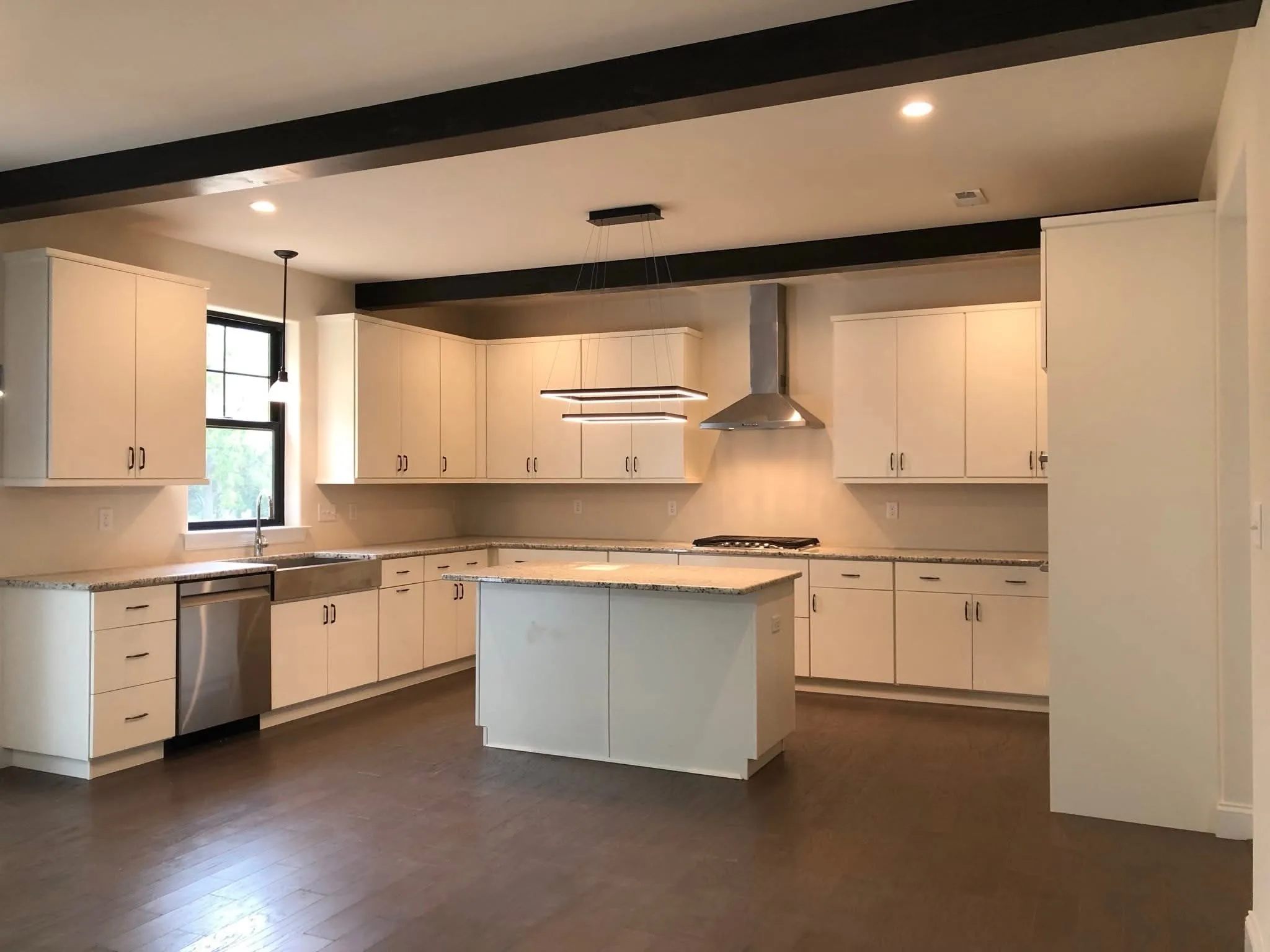 A modern kitchen featuring white shaker cabinetry, a central island, and dark exposed ceiling beams.