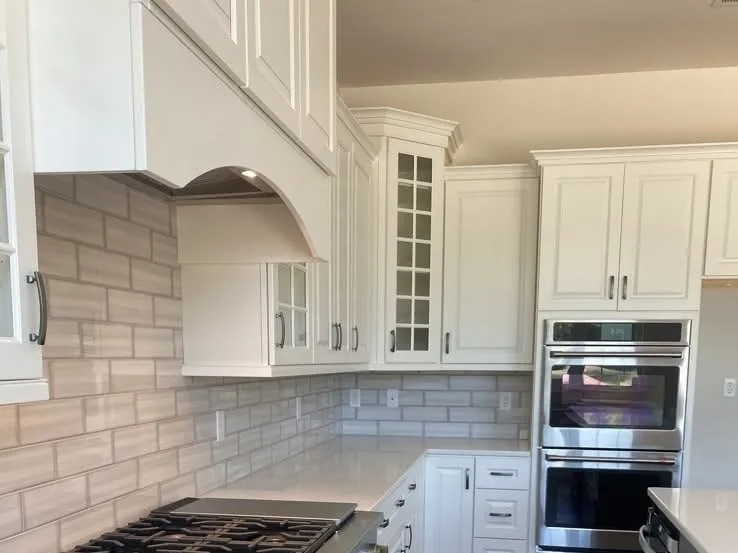 White shaker style kitchen cabinets with a arched range hood and glass door accents.