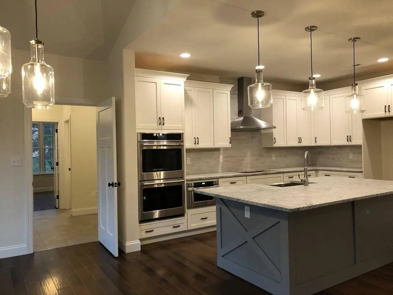 A kitchen featuring white shaker cabinets, a grey island with x-panel detail, and glass pendant lights.