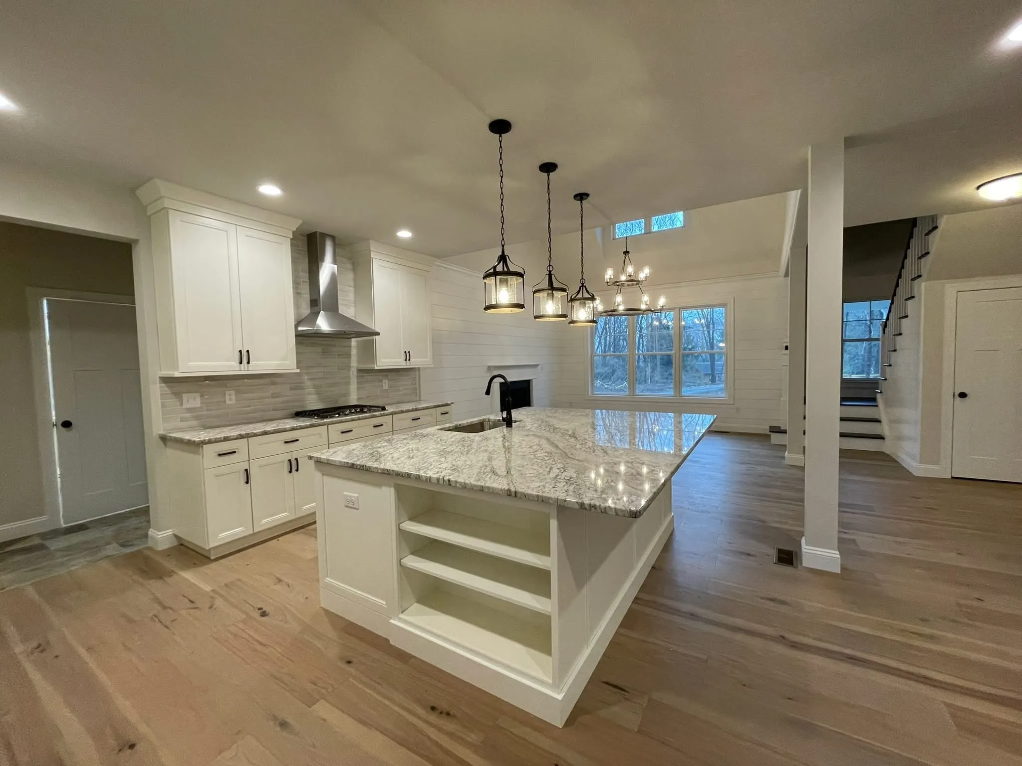 A white shaker kitchen features a large granite island with open shelving and pendant lighting.