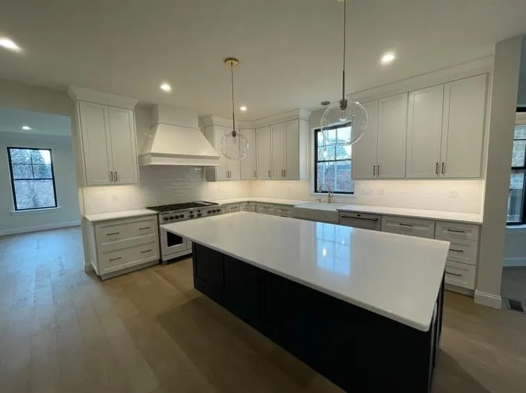 White shaker cabinets with a large navy blue kitchen island and quartz countertop in a kitchen.
