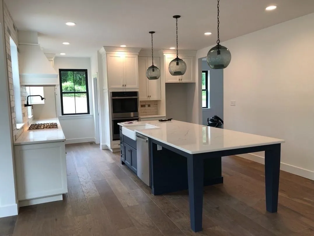 A modern kitchen features white shaker cabinets, a navy blue island, and glass pendant lights.
