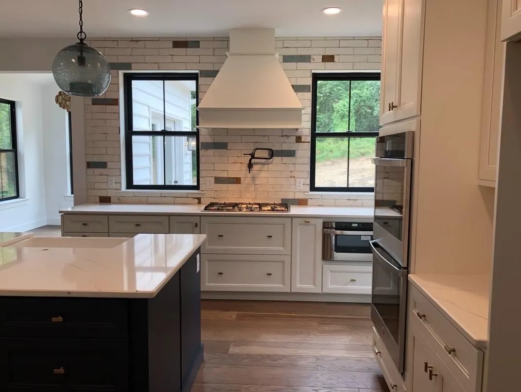 A white shaker kitchen with a dark navy island and a range hood surround.