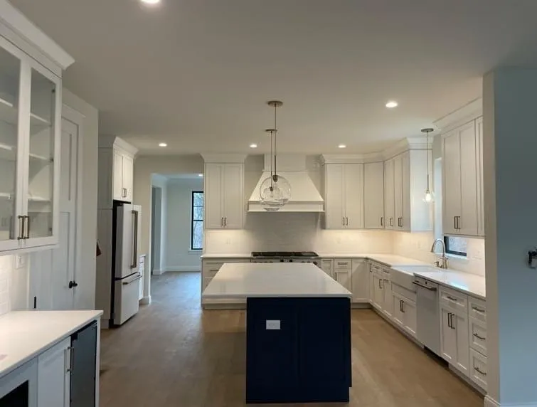 A white shaker style kitchen features a navy blue center island and white quartz countertops.