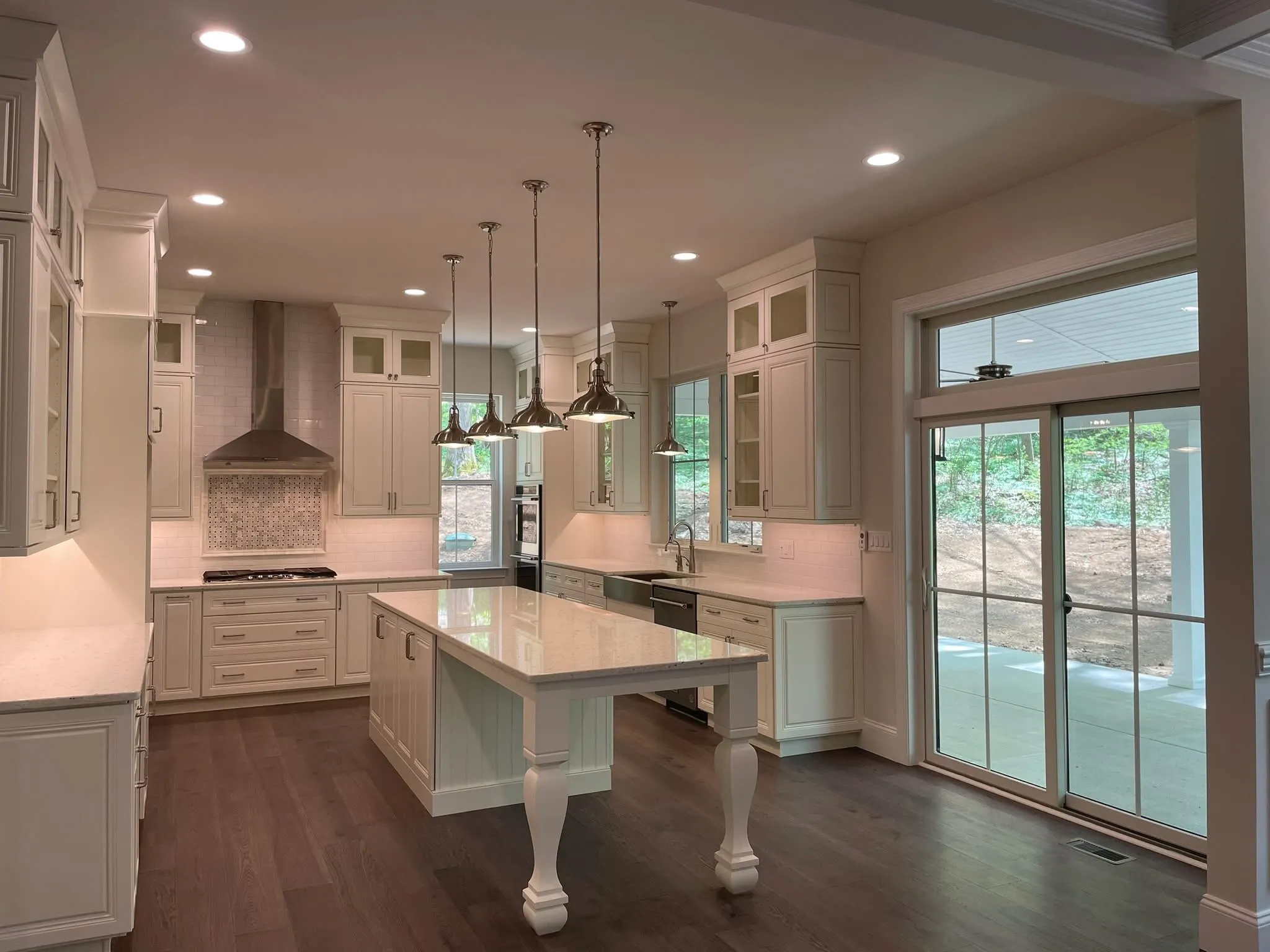 A white shaker style kitchen features a large central island with turned legs and pendant lighting.