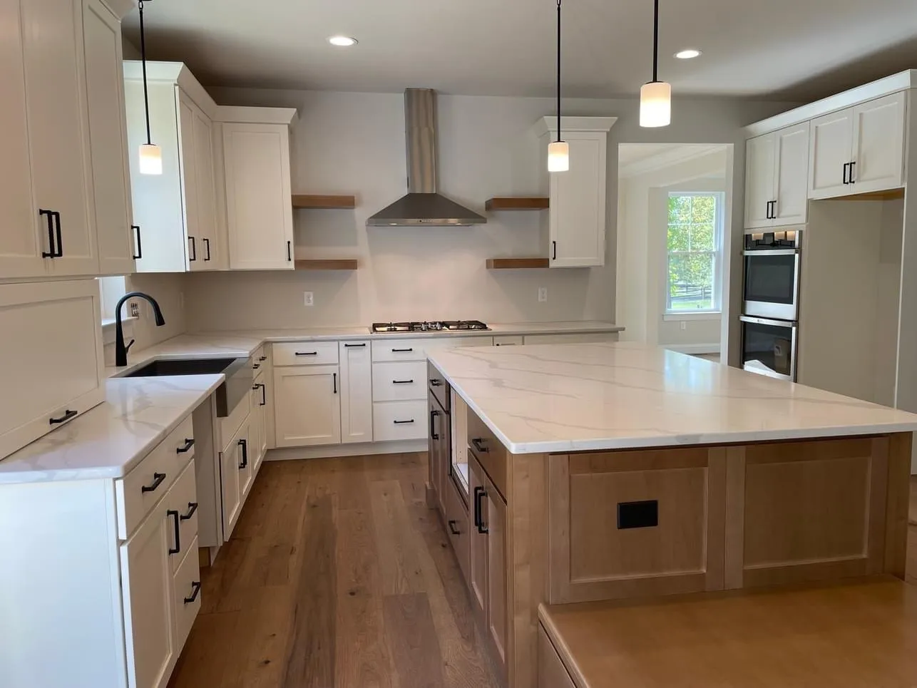 A modern kitchen featuring white shaker cabinets, a large wood island, and floating wooden shelves.