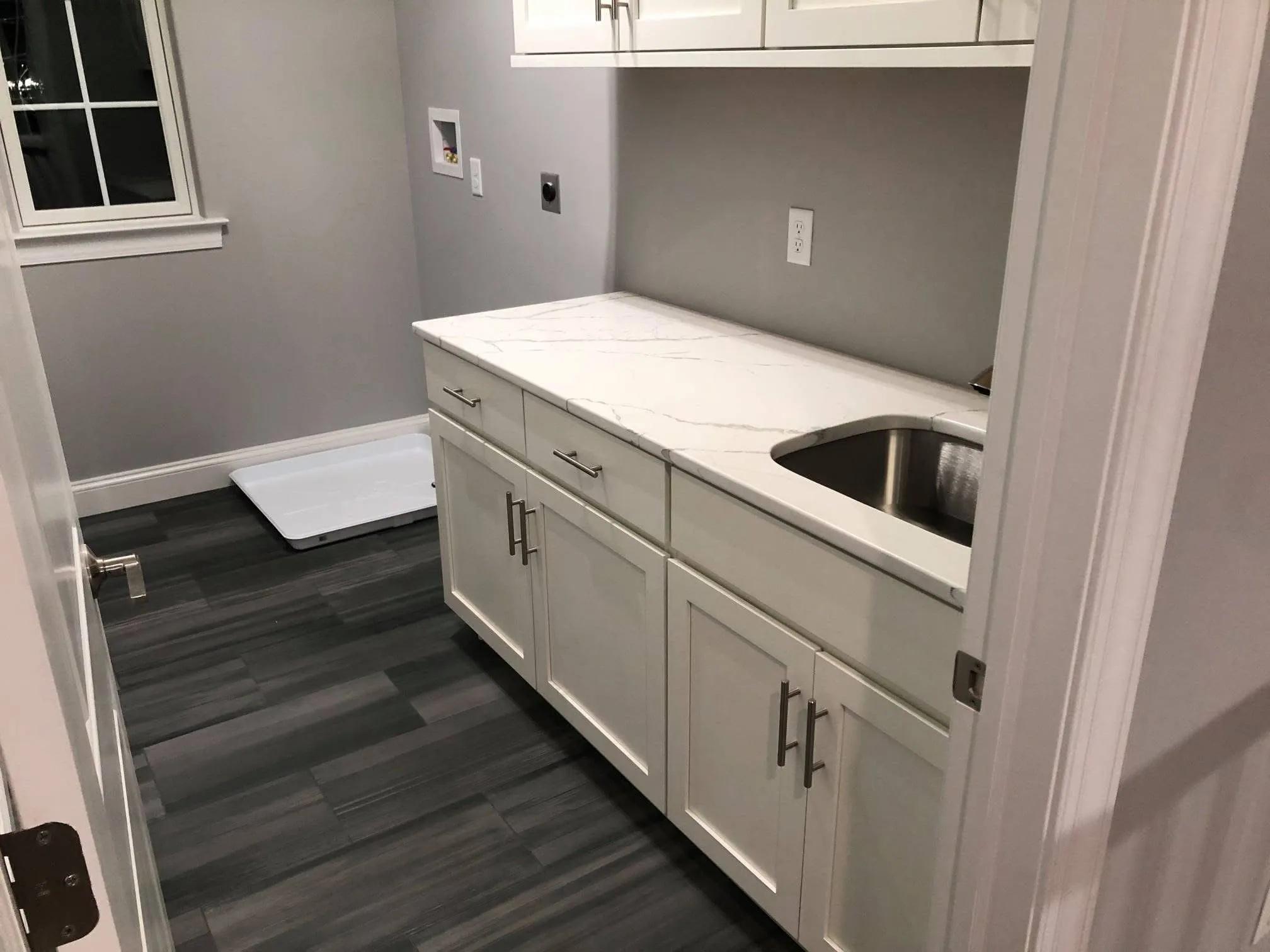 White shaker style cabinets with a marble countertop and sink installed in a laundry room.