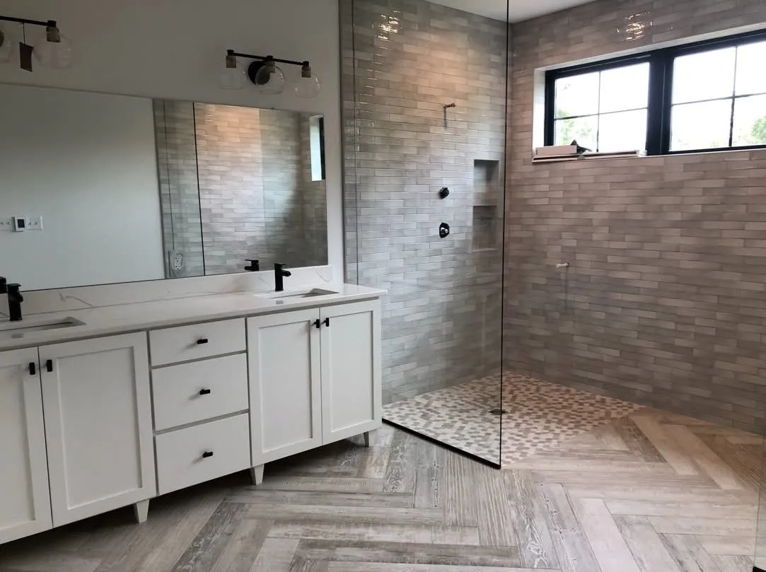A white shaker style double vanity sits beside a glass enclosed walk-in shower with tile.