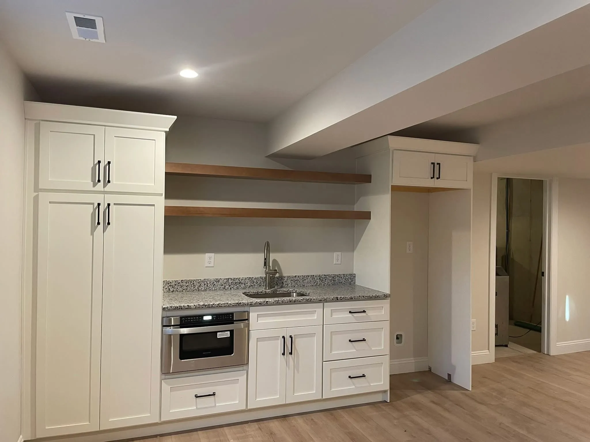 White shaker style wet bar cabinetry featuring floating wood shelves and a granite countertop.