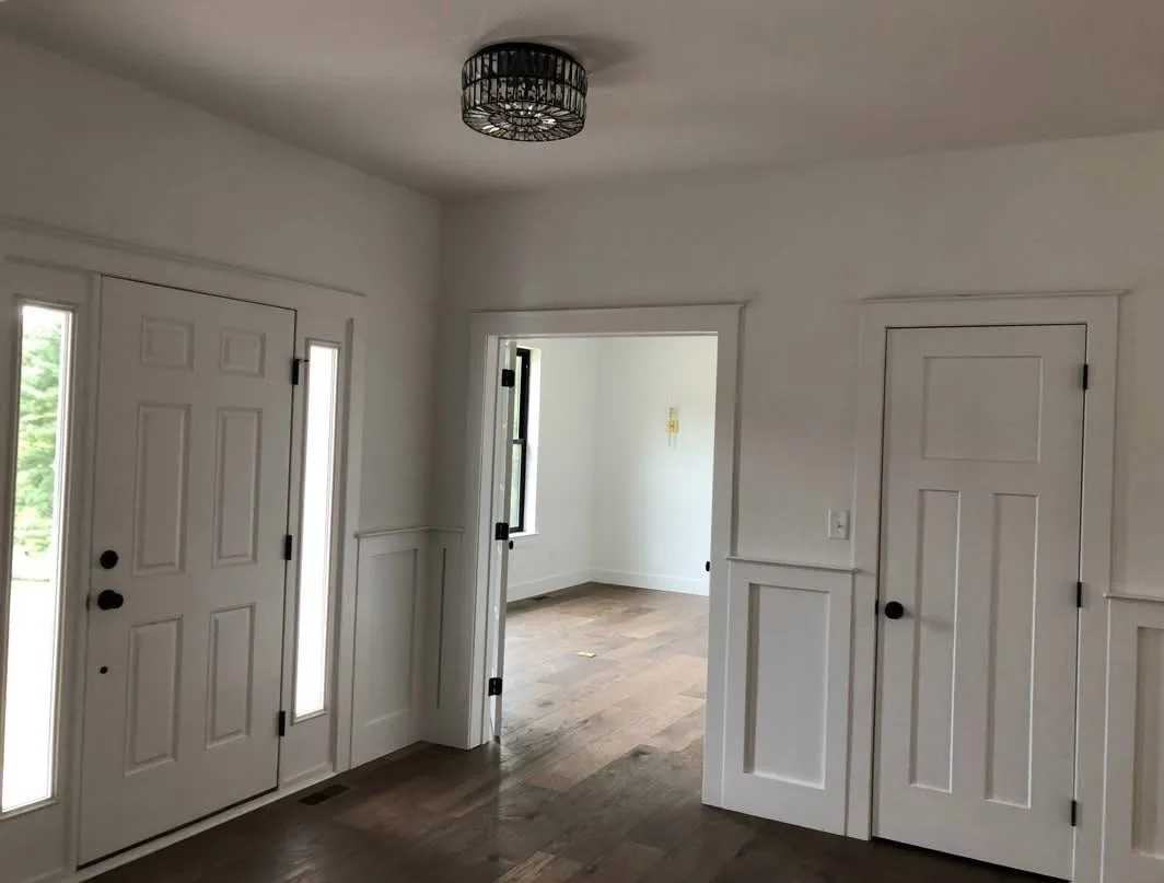 White wainscoting and door casing installed in a bright entryway with hardwood flooring.